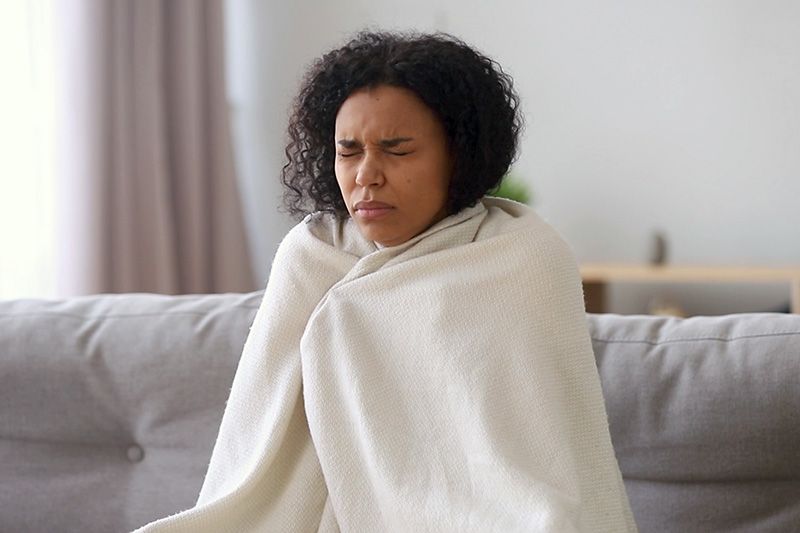 Upgrade Your Furnace. Image shows woman sitting on couch and wrapped in blanket.
