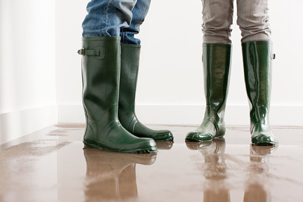 People wearing rain boots on a flooded floor. Why Is My Furnace Leaking Water?