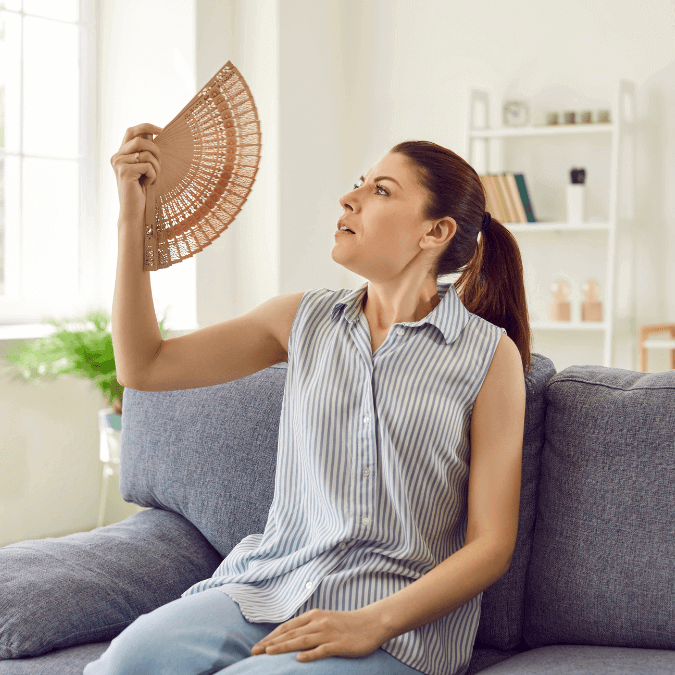 Woman on couch waving fan to ward off summer heat